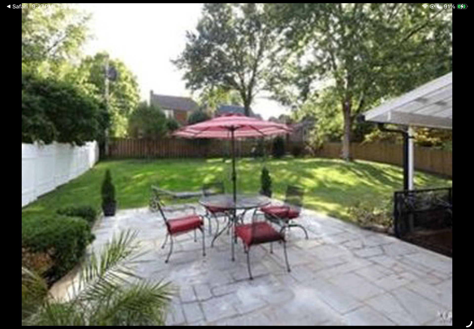 Stone patio with umbrella table and red cushioned chairs overlooking the lawn