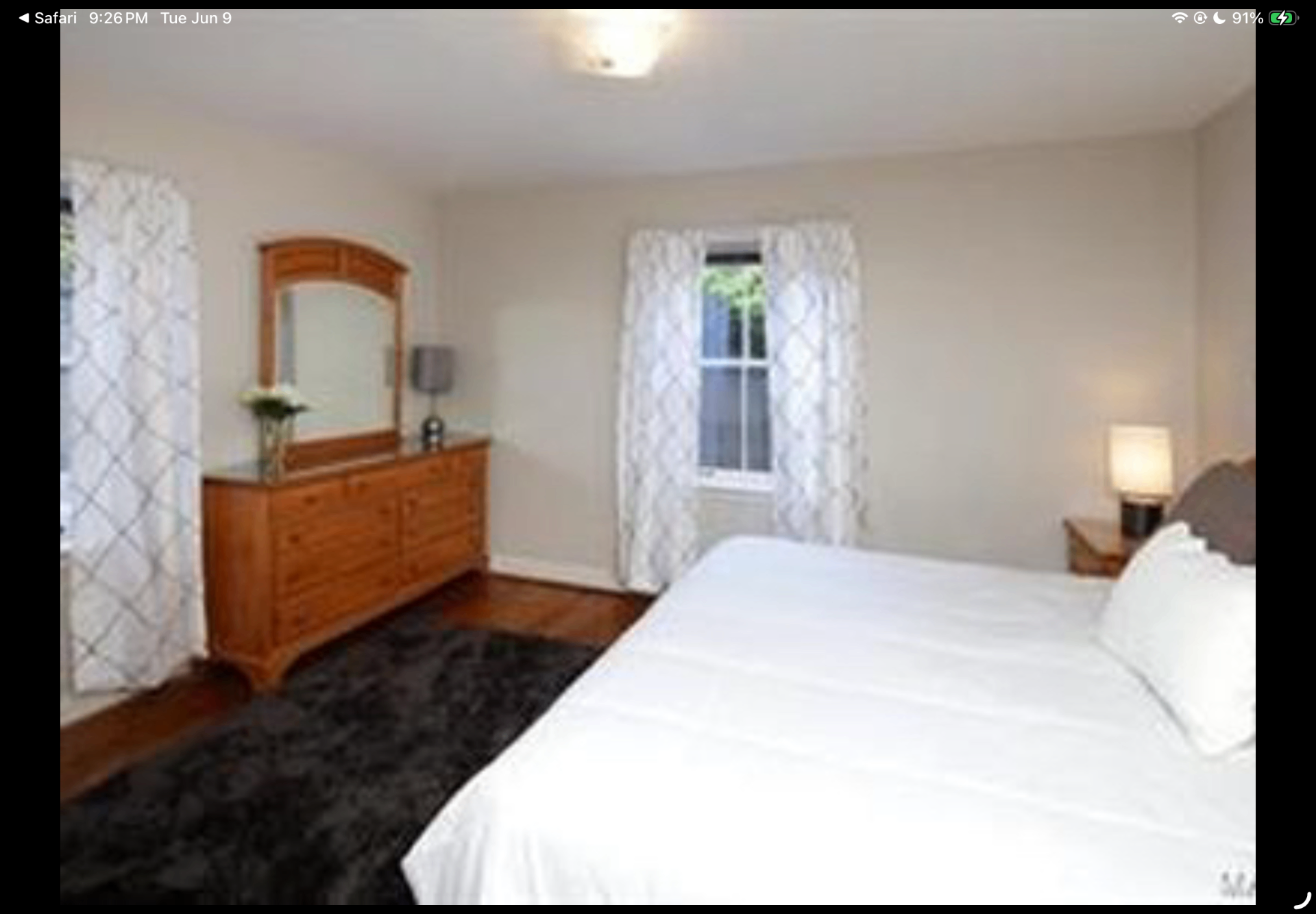 Primary bedroom with wood dresser, patterned curtains and bright white bedding