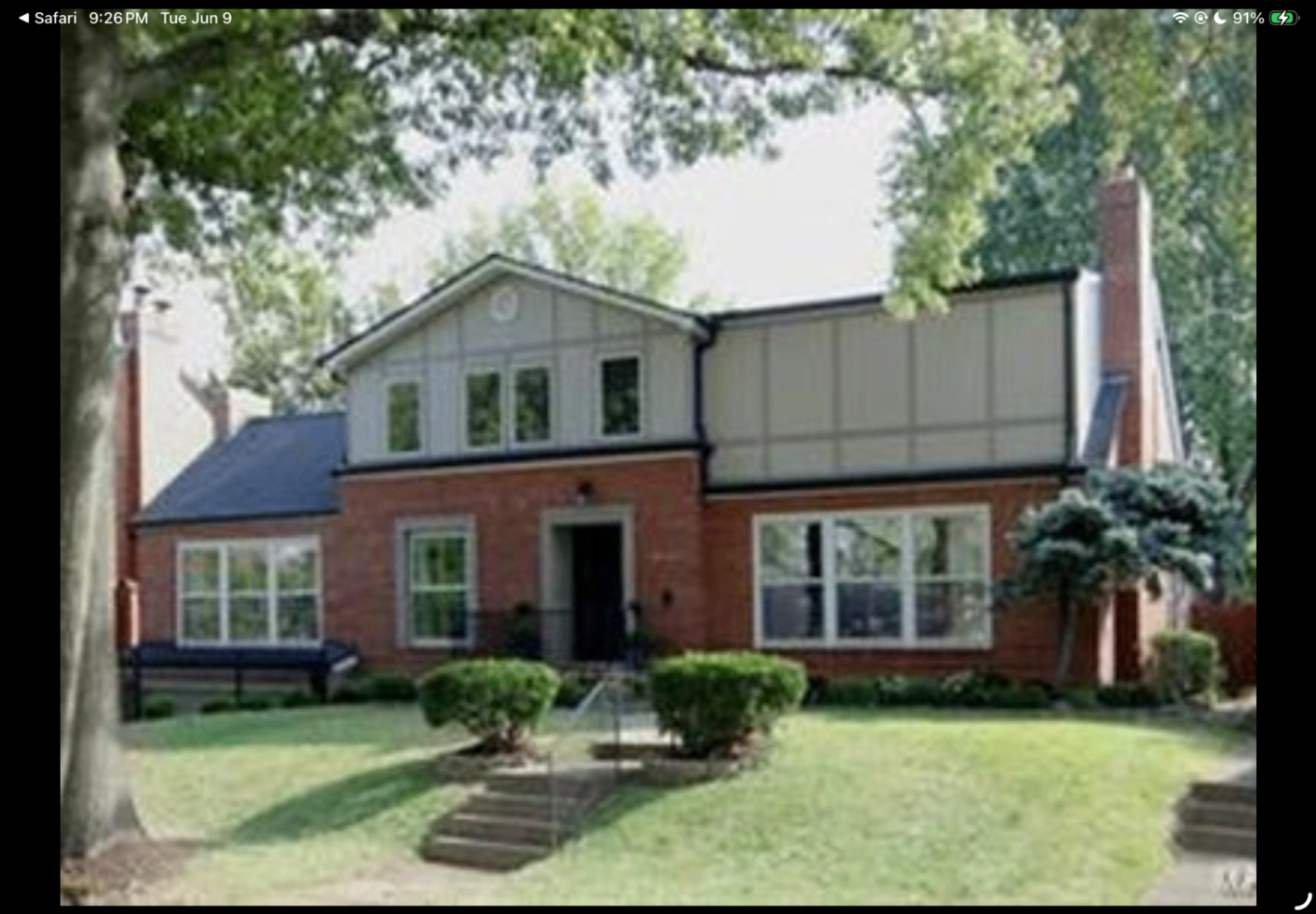 Front exterior view of a two-story brick home framed by mature trees