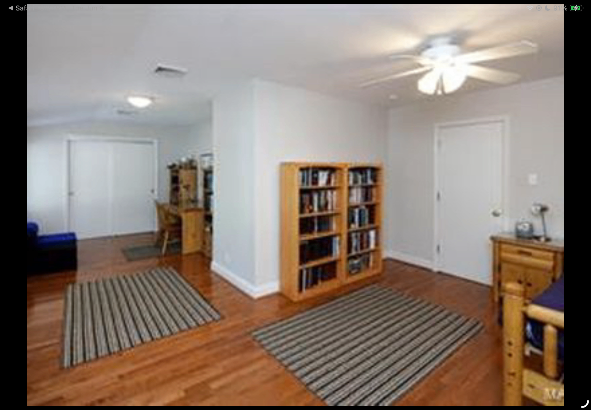 Open lower-level room with striped rugs, bookcases and hardwood flooring